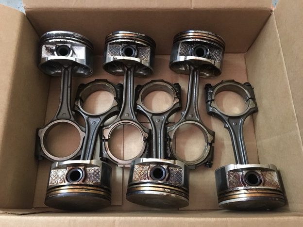 Six piston-and-connecting-rod assemblies arranged in two rows in a cardboard box.