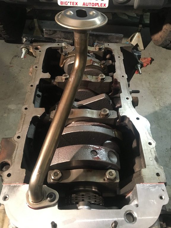 Underside of the engine with its crankshaft, bearing caps, and oil pickup tube exposed.