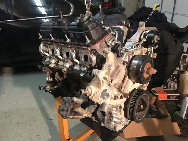 Angled view of the partly assembled V6 on an orange engine stand with a lifting chain attached.